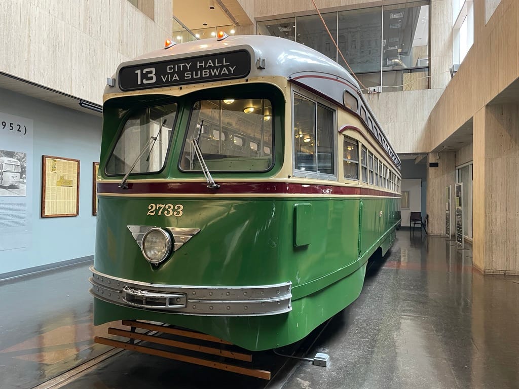 A green trolley car with a silver headlight. The number board says "13 City Hall via Subway"