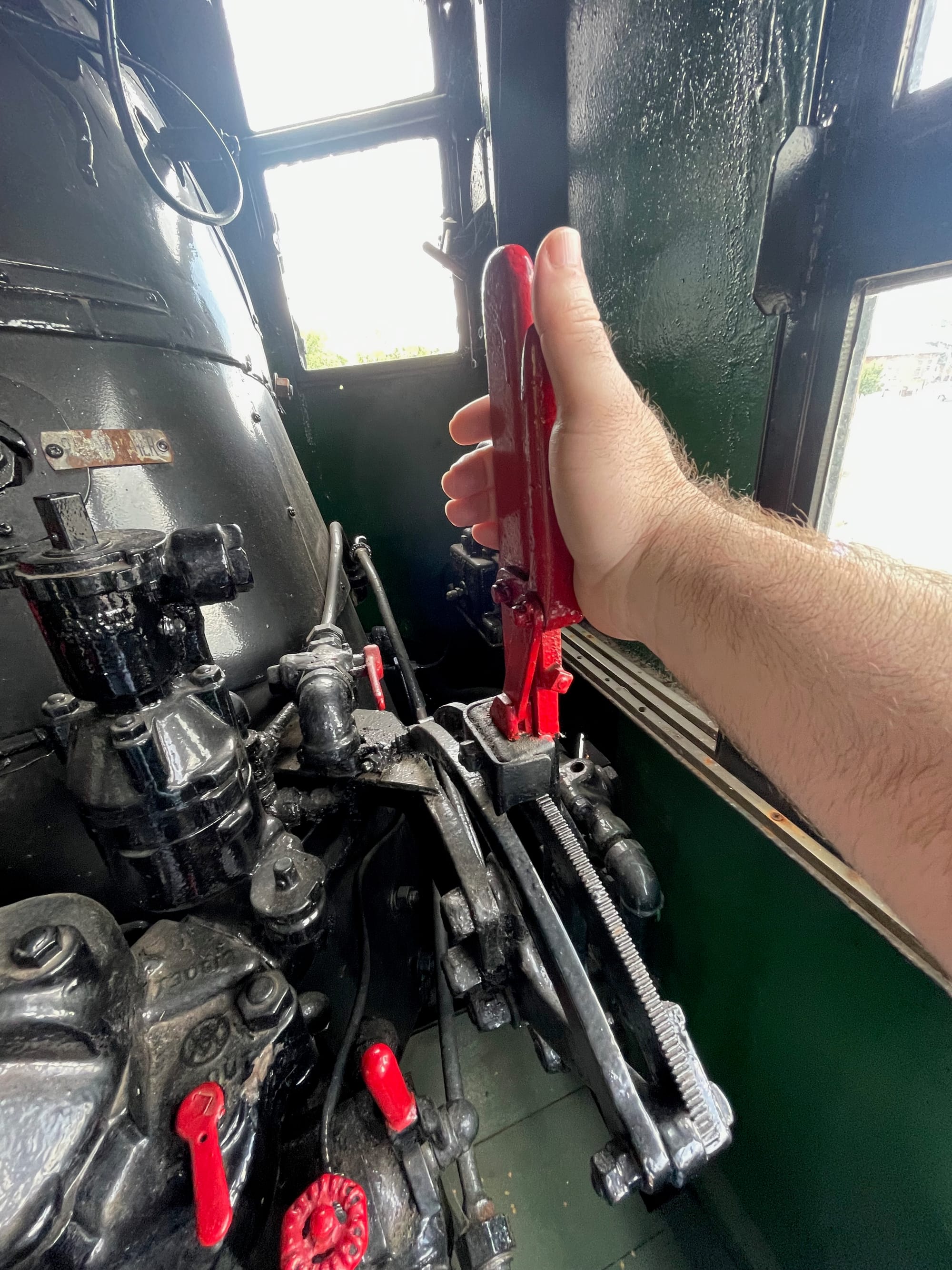A person holding a red handle that controls a steam locomotive. There are other red handles and valves on black control services