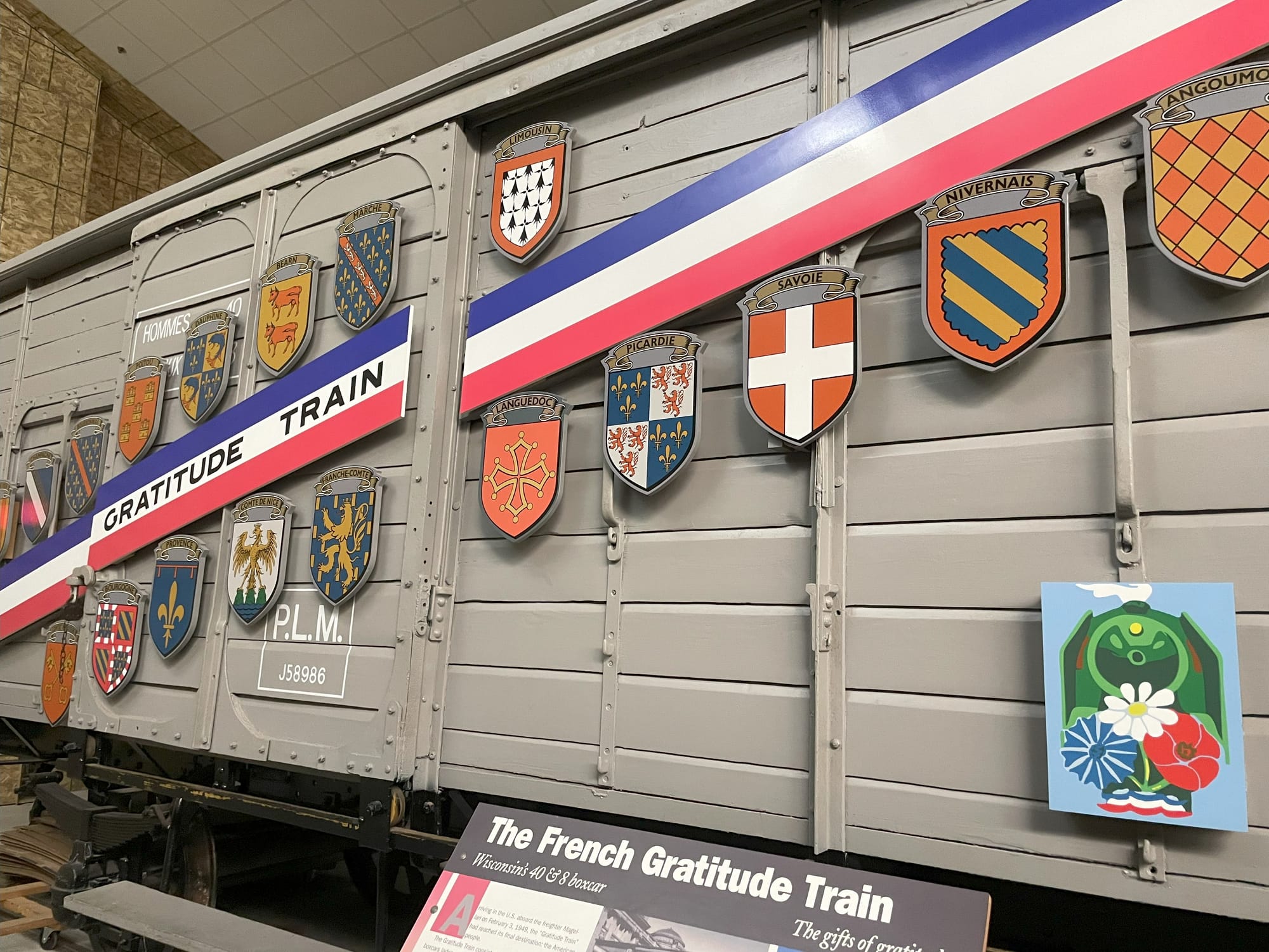 A gray boxcar with a red white and blue banner across it, along with several family crests. The words on the banner say "Gratitude Train"