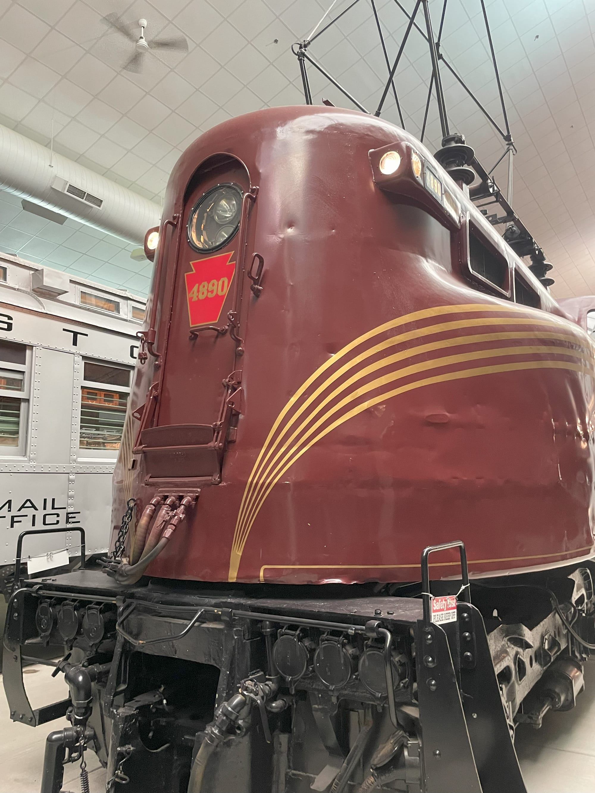 A brown electric locomotive with a gold stripe. The nose is high with a single round headlght at the top. The pantograph is raised