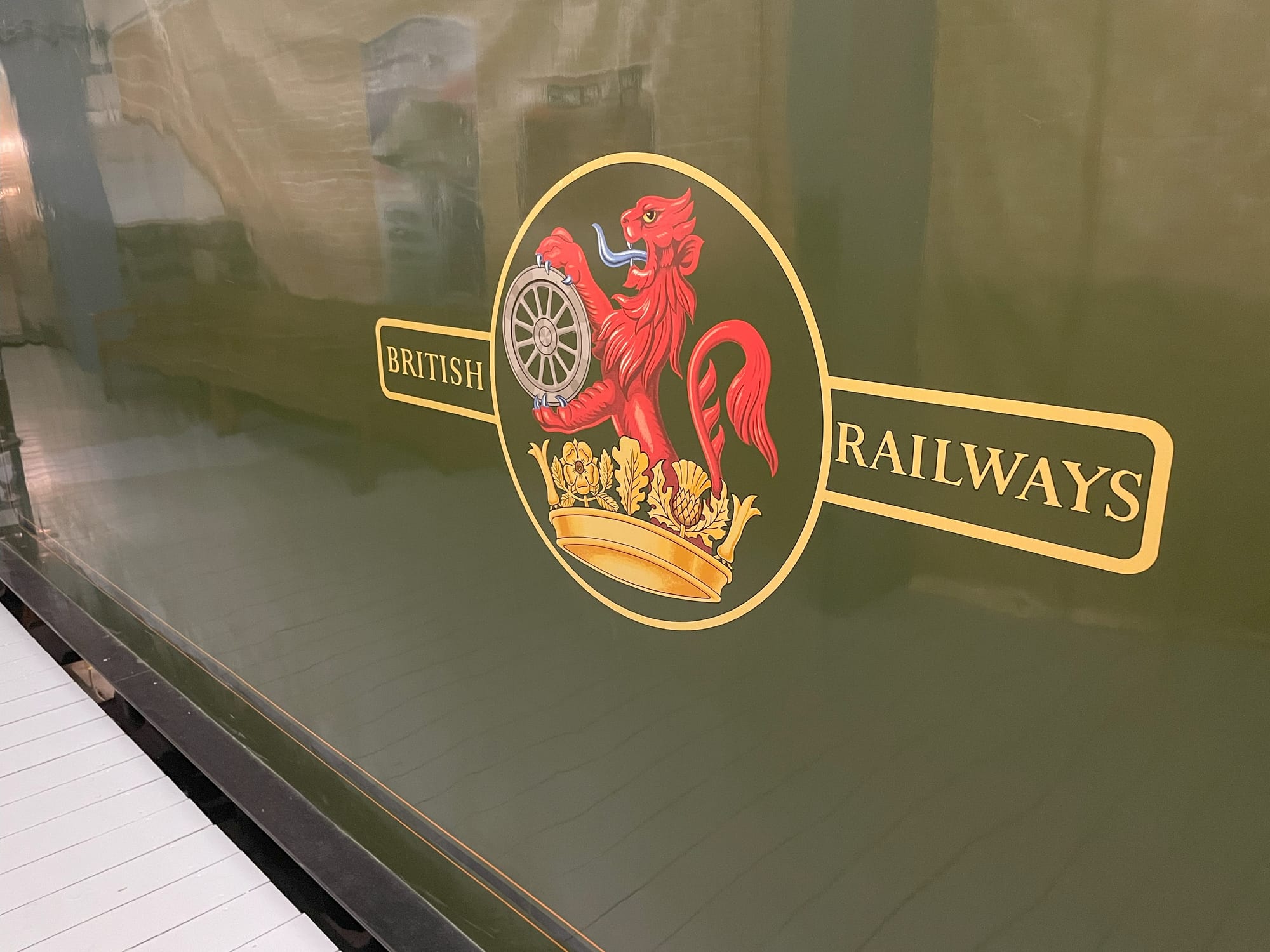 The green side of a locomotive tender. There's a red dragon holding a locomotive wheel standing on a gold crown the logo is in a gold circle. On either side of the circle reads "British" and "Railways" outlined with a gold border