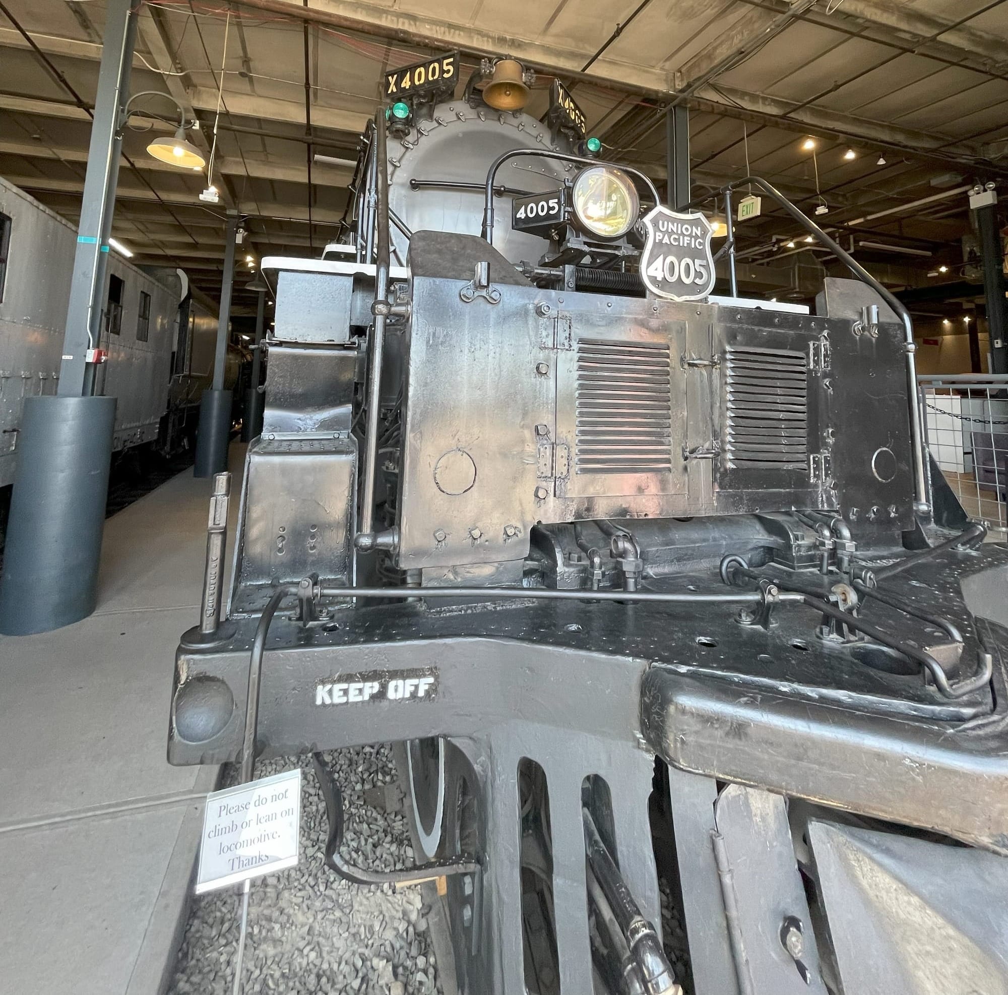 A Big Boy Steam locomotive front view. In the foreground the black cowcatcher with the Union Pacific shield reading 4005 in black and silver mounted above. Above the shield is the headlight in front fo the silver boiler with the bronze bell mounted over the top