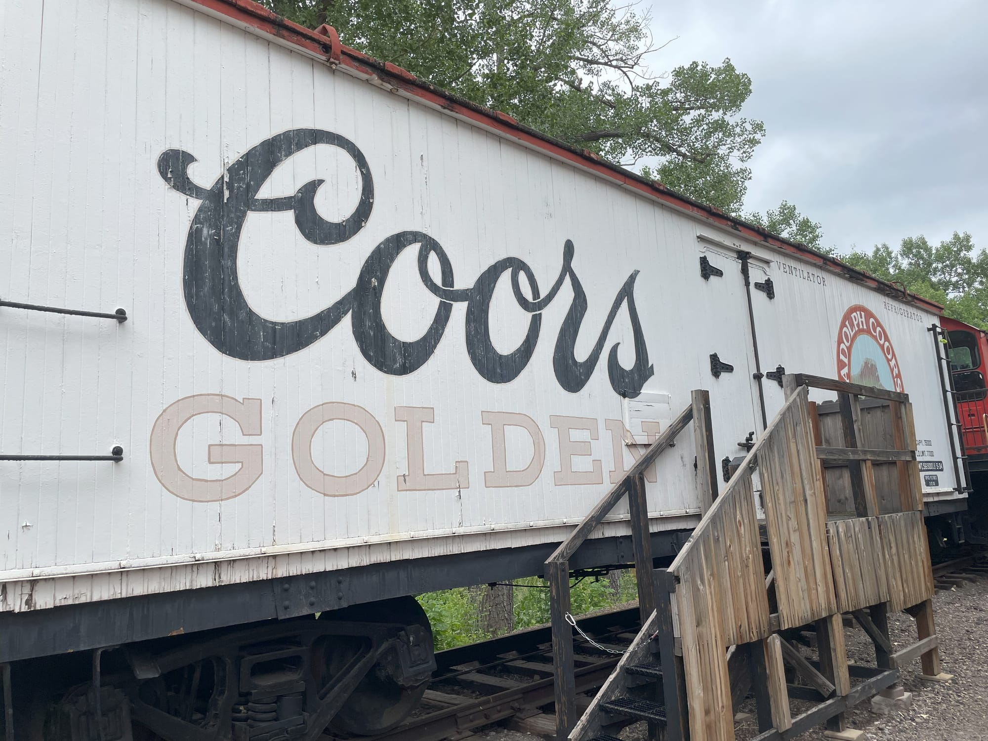 A white refrigerated box car with a large Coors beer logo and the city name Golden written in block gold letters underneath.