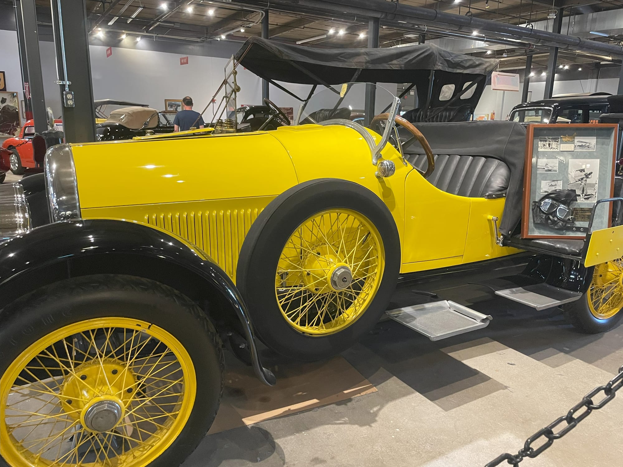 A yellow and black roadster style car with yellow spoked wheels and a chrome grill. Looking from the side you can see the wooden steering wheel