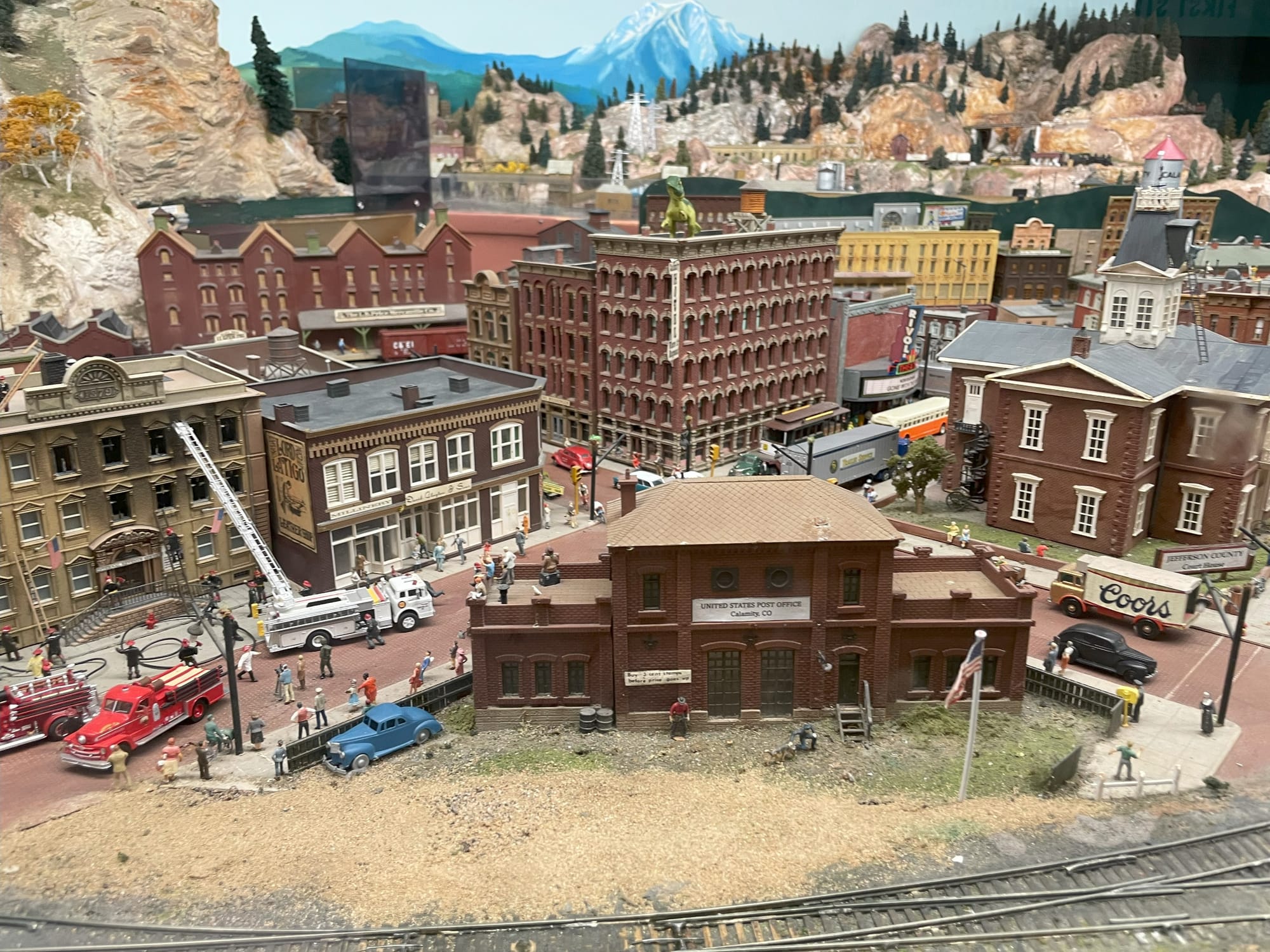 A model city scene. There's a fire truck and fire fighters putting out flames in a building. The background is a painted mountain.