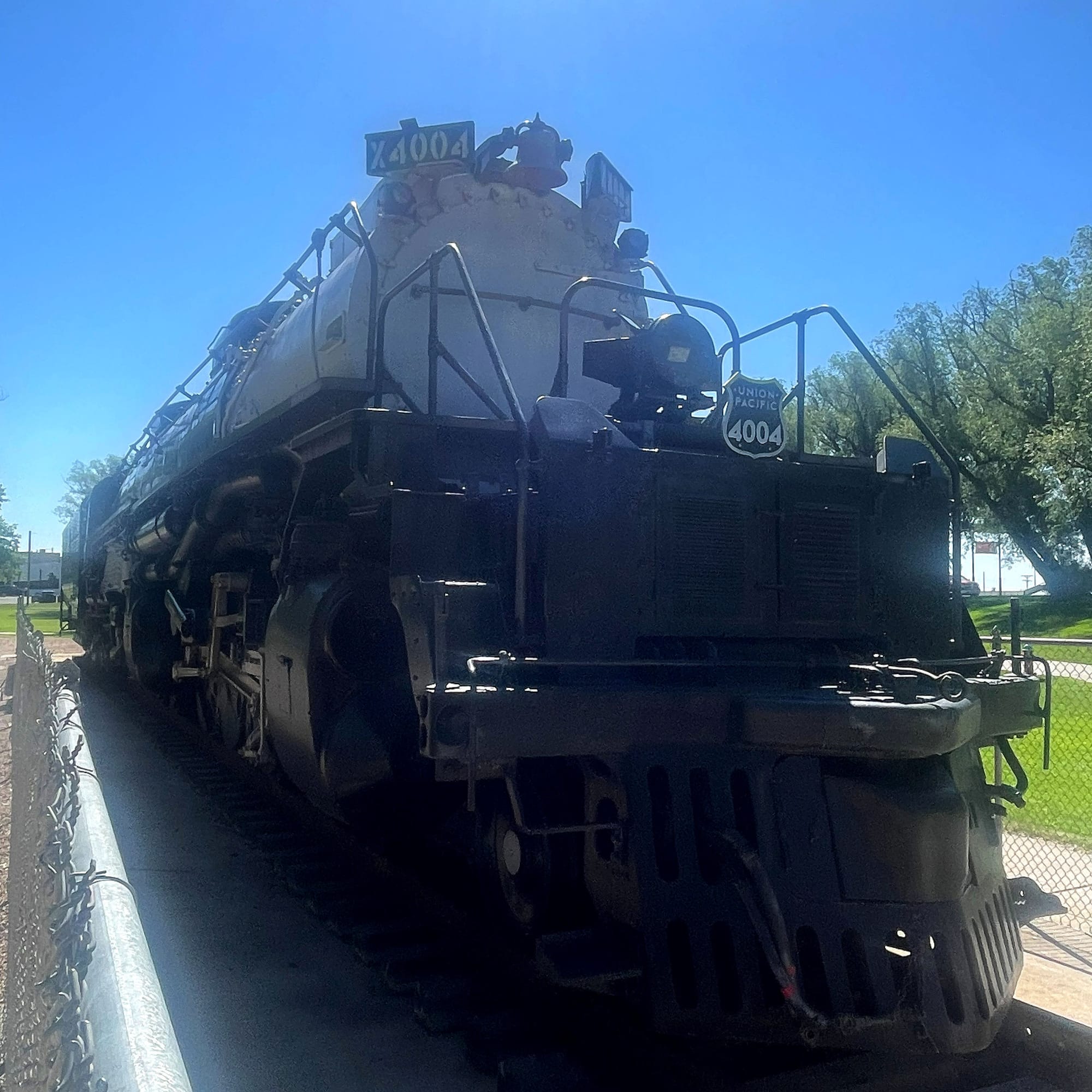 A steam locomotive in the sun. The boiler is silver and the nunber board says 4004