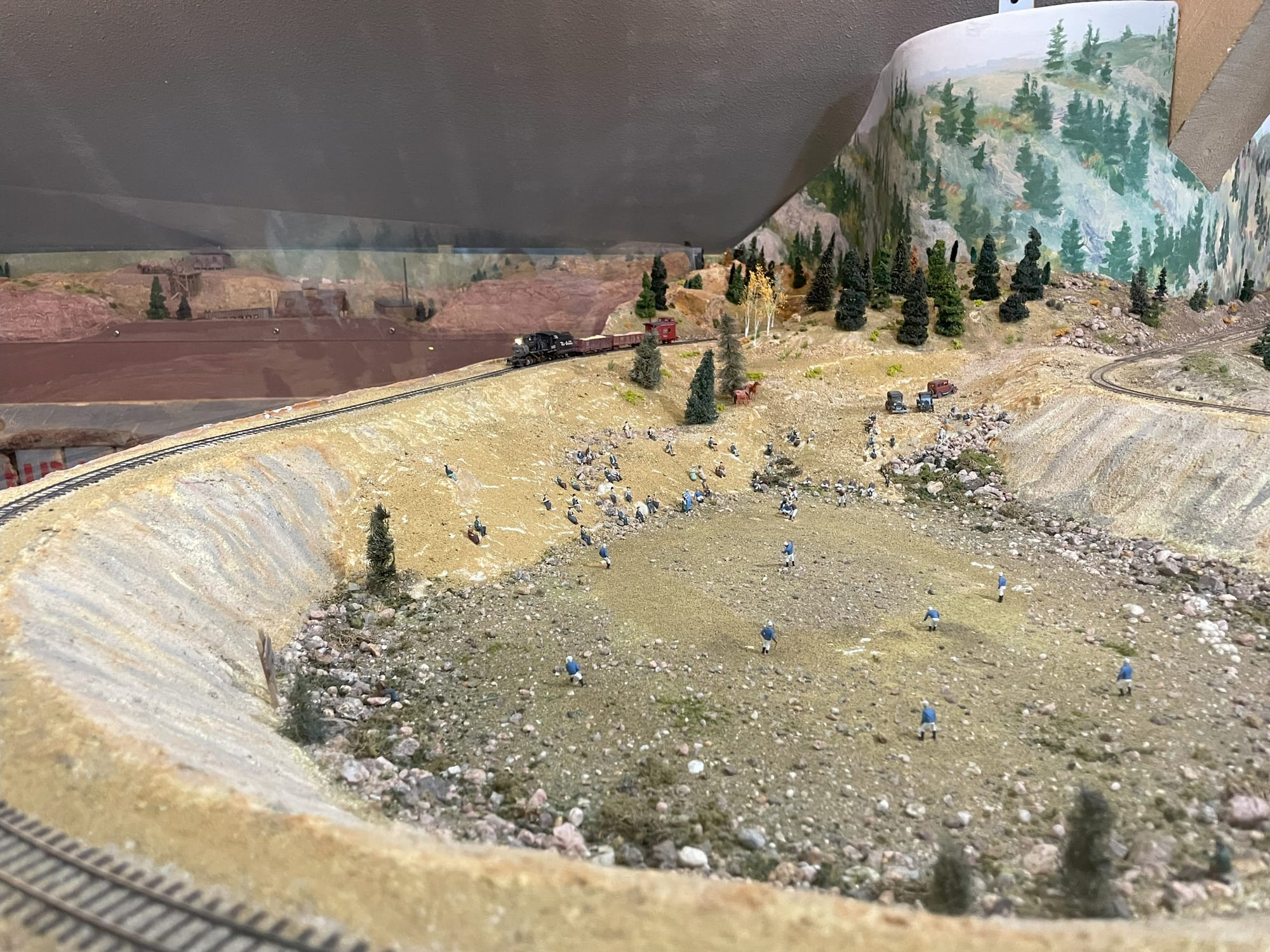 A model railroad setup with figures playing baseball in the foreground and a train in the background, in front of a mountain