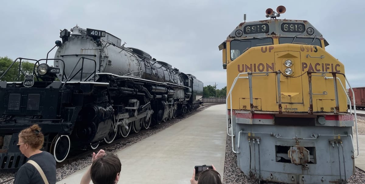 A black and silver steam locomotive, next to a yellow and gray Union Pacific diesel-electric locomotive