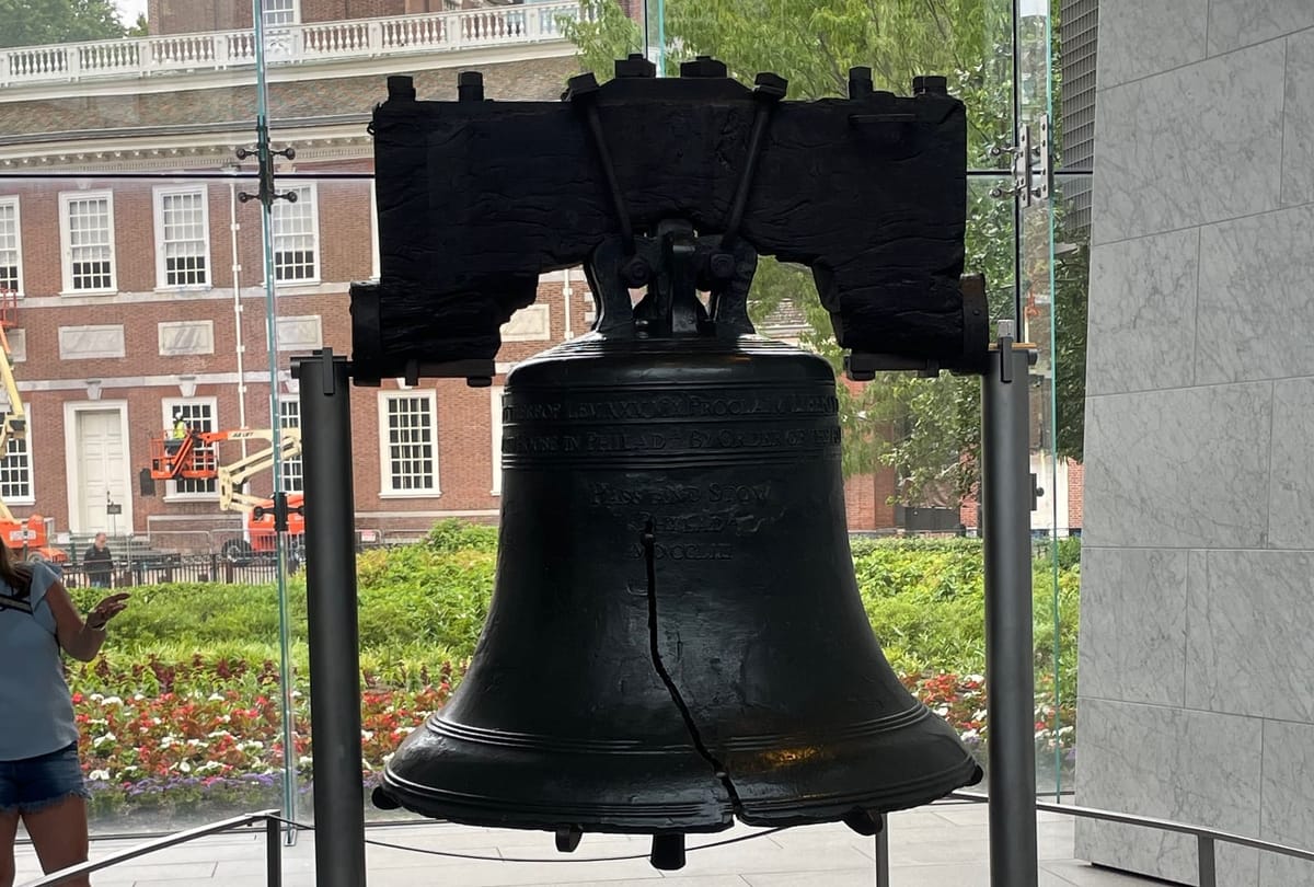 A large black bell on a stand. The bell has a crack starting from the lip and about halfway up.