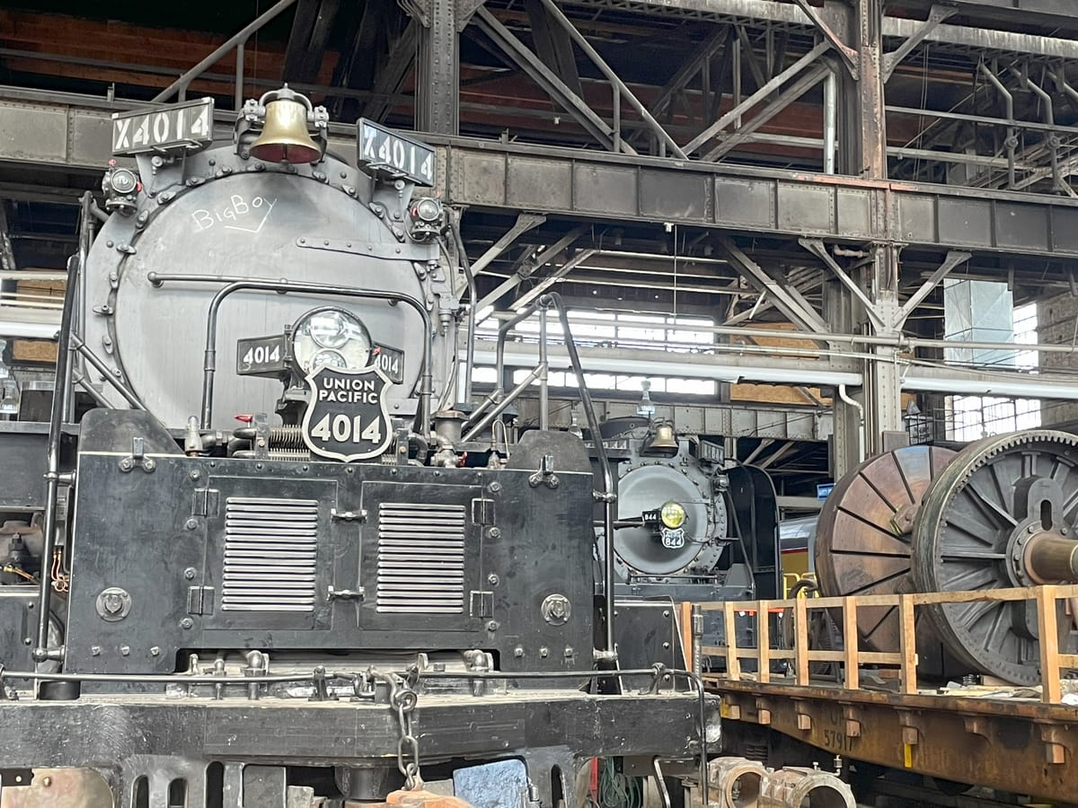 A pair of steam locomotives. Foreground 4014 in gray and sliver. Background 844 in gray and sliver. There's a flatcar with equipment in front of 844.